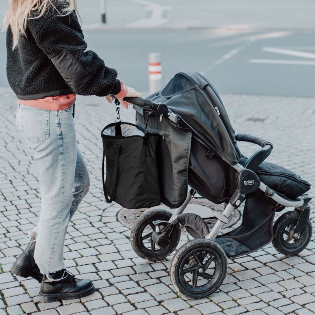 Wickeltasche Greta hängend am Kinderwagen. Schwarze Wickeltasche mit montierbarer Kinderwagenaufängung zum Tragen oder Anhängen von Anna und Oskar